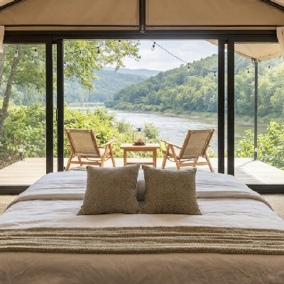 Tent bedroom with white linen bed facing open deck chairs overlooking a jungle river.