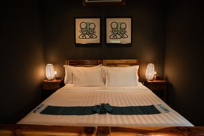 Cozy guest room at The Namkhan in Luang Prabang featuring wooden furniture, warm bedside lamps, local artwork, and crisp white linens.