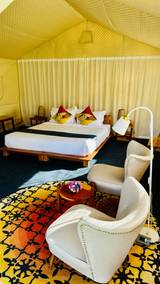 Interior of a canvas tent at The Namkhan in Luang Prabang showing white seating, patterned rug, wooden platform bed, and yellow quilted ceiling