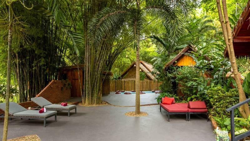Secluded pool deck surrounded by bamboo and tropical palms, featuring sun loungers with coral cushions and traditional teak pavilions