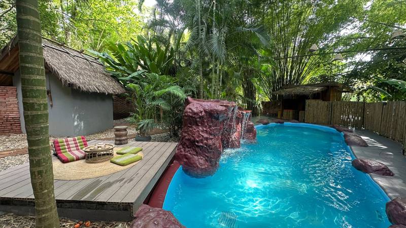 The Namkhan resort pool with cascading waterfall feature and tropical lounge deck surrounded by lush gardens in Luang Prabang, Laos