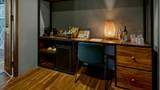 A teak wood desk with rattan lamp, teal chair, and minibar in a hotel suite.