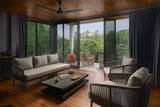 Spacious villa living area at The Namkhan in Luang Prabang featuring contemporary furnishings, warm wood finishes, and floor-to-ceiling windows opening to pr...