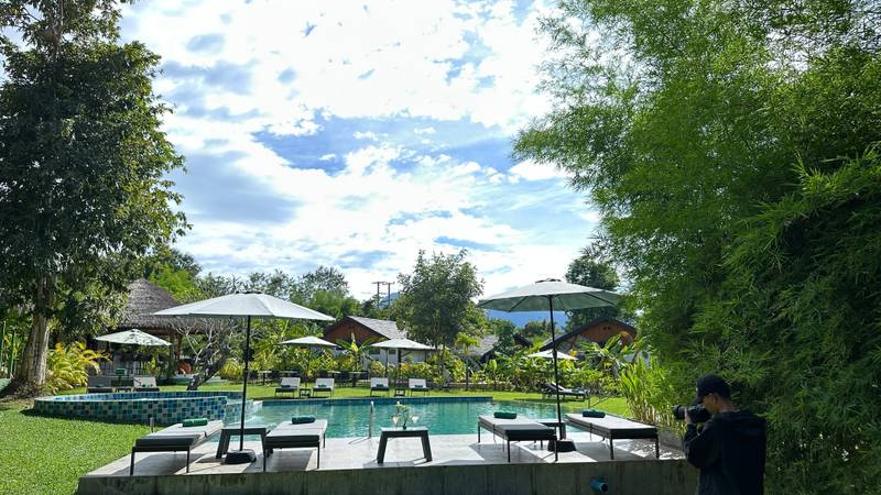 Pool lounge area with sun loungers and umbrellas at The Namkhan resort in Luang Prabang, surrounded by lush tropical gardens and traditional Lao villas