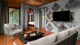 A grey-walled villa living room with damask wallpaper, teak floors, and an arched bedroom doorway.