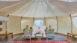 Interior of a round glamping tent with a white bed, floral armchairs, and woven rugs.