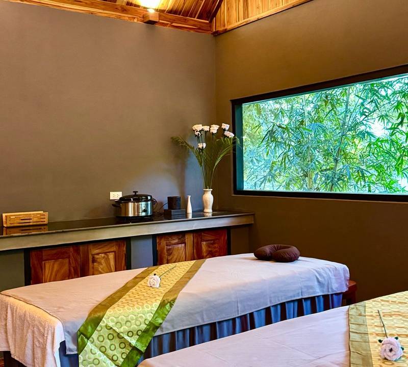 Tranquil spa treatment room at The Namkhan in Luang Prabang, featuring twin massage beds, bamboo forest views, and natural teak ceiling