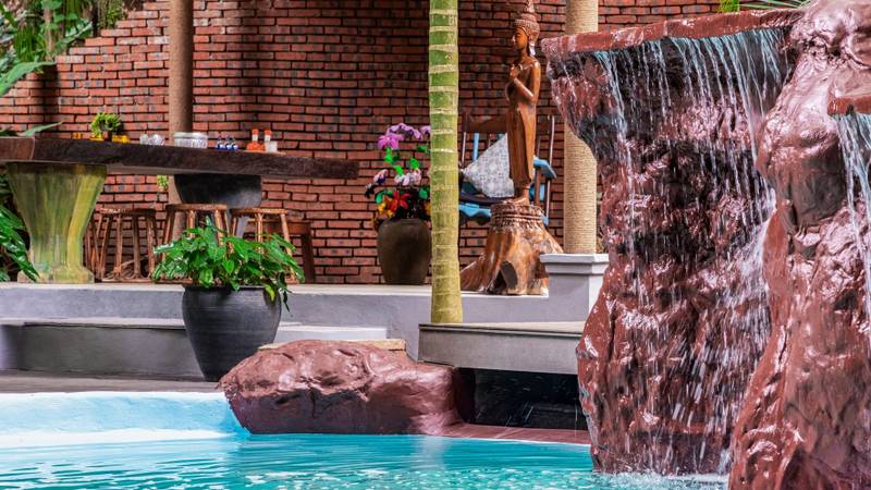 Cascading waterfall feature at The Namkhan resort pool with traditional brick pavilion and Buddha statue in Luang Prabang, Laos