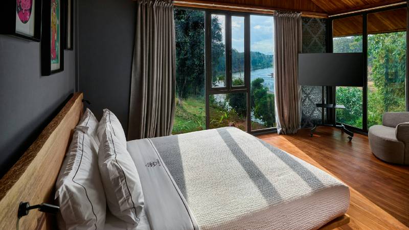 A neatly made bed faces floor-to-ceiling glass doors opening toward the Namkhan river and jungle.