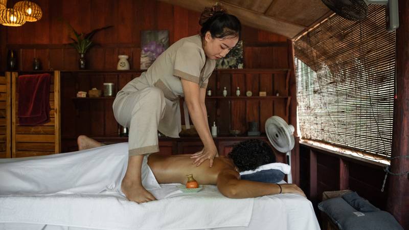 Therapist performing traditional massage treatment in wooden spa room at The Namkhan, Luang Prabang, with natural light and local decor