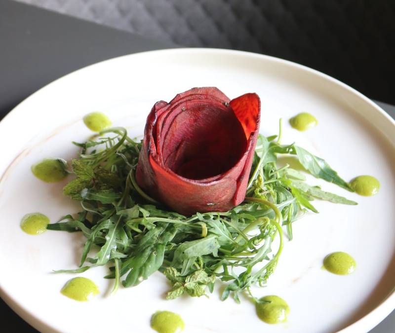 Artisan salad featuring beetroot rose garnish with fresh arugula and herb oil dots on ceramic plate at Namkhan riverside restaurant
