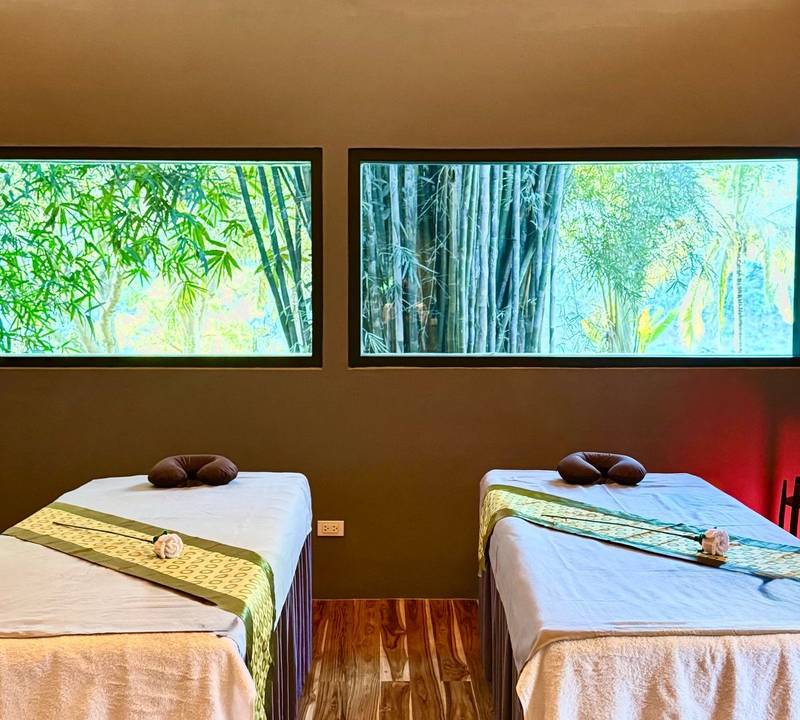 Couple spa treatment room at The Namkhan in Luang Prabang featuring twin massage beds with bamboo garden views through floor-to-ceiling windows