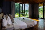 Spacious riverside villa bedroom at The Namkhan in Luang Prabang featuring floor-to-ceiling windows with panoramic river views and natural wood interiors