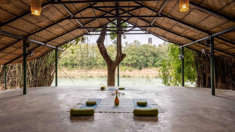 Open-air yoga pavilion at The Namkhan in Luang Prabang with meditation cushions, natural bamboo ceiling, and peaceful river views