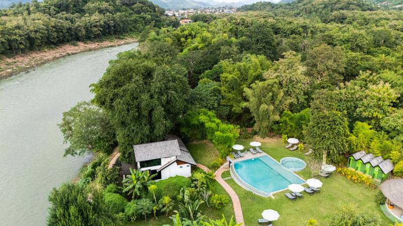 Aerial view of The Namkhan resort pool with lounge chairs and tropical gardens along the riverbank in Luang Prabang, Laos