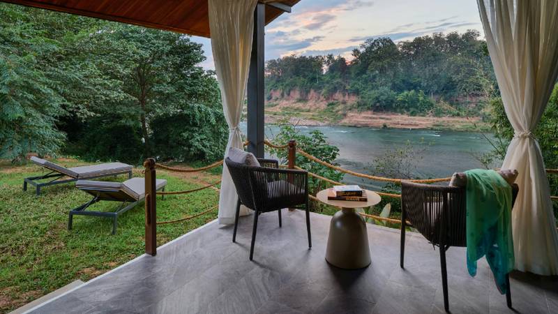 A terrace with rope chairs and side table overlooking the Namkhan River at dusk.