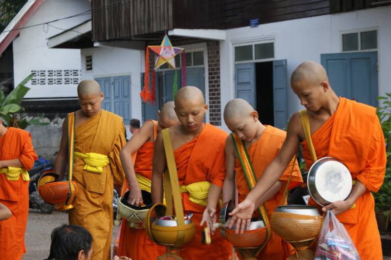 Buddhist monks in orange robes collecting alms in traditional ceremony near The Namkhan resort in Luang Prabang, Laos