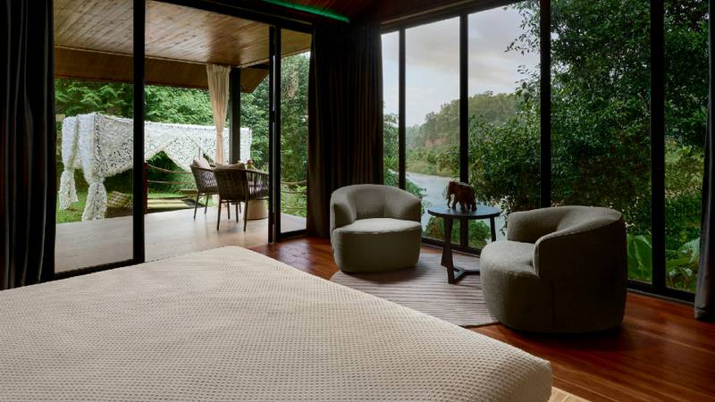 Riverfront suite interior with lounge chairs, glass walls, and jungle river view.
