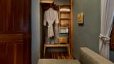 Open wardrobe with hanging linen robe, wicker baskets, and wooden slippers on a bench.