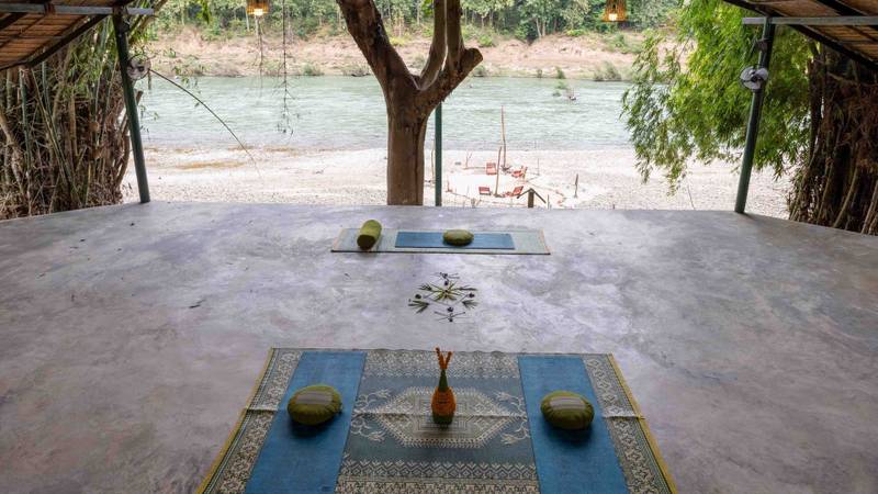 Open-air yoga pavilion at The Namkhan resort in Luang Prabang, featuring meditation mats overlooking the tranquil Nam Khan River.