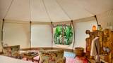 Interior of a canvas glamping tent with floral chairs, rattan basket, and jungle window view.