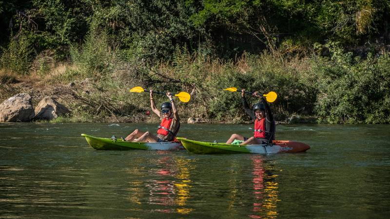 Two people in life jackets paddling kayaks on a calm green river.