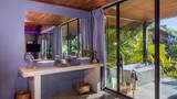 A concrete double vanity with grey curtains and floor-to-ceiling glass overlooking lush jungle.