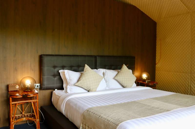 King bed with tufted leather headboard and warm bedside lighting in guest room at The Namkhan, Luang Prabang, featuring woven wall textures
