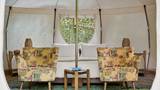 Interior of a glamping tent with two floral armchairs and a white canopy bed.