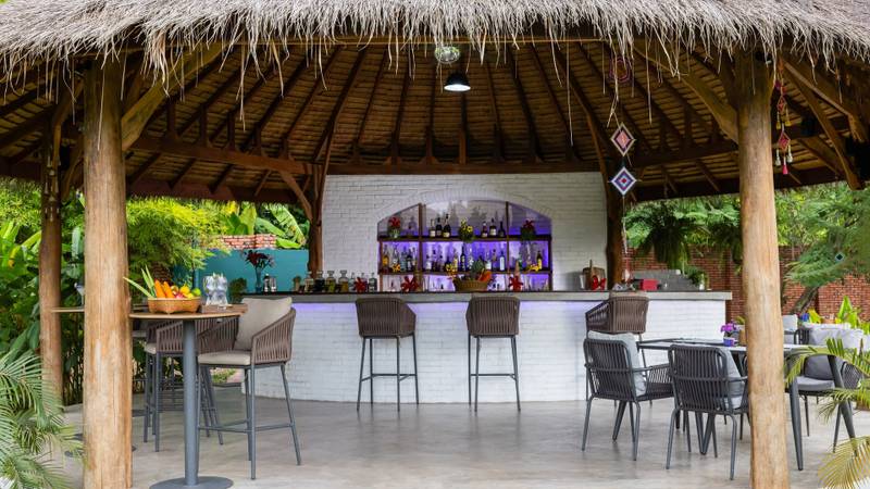 Open-air pool bar at The Namkhan in Luang Prabang featuring thatched roof pavilion, modern seating, and lush tropical garden surroundings
