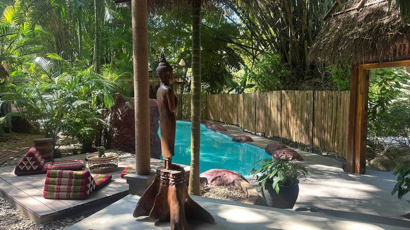 Serene pool surrounded by tropical gardens and traditional Buddha statue at The Namkhan resort in Luang Prabang, Laos with bamboo fencing