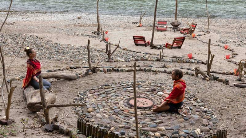 Two guests in traditional dress sit peacefully within a stone labyrinth meditation garden beside the Nam Khan River, wooden loungers beyond
