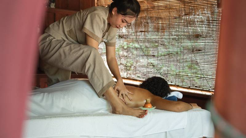 Traditional Lao massage therapy session in the spa treatment room at The Namkhan eco-resort, Luang Prabang, featuring natural materials and river views