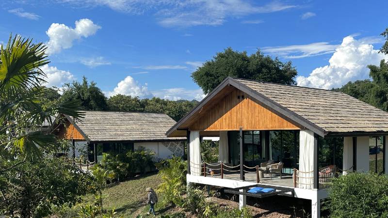 Wooden pavilion building with shingle roof surrounded by lush garden, child walking in foreground.