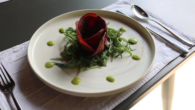 Elegant beetroot rose garnish on fresh arugula with green herb coulis, plated on cream ceramic at Namkhan riverside restaurant table