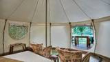 Interior of a circular glamping tent with floral armchairs, a bed, and a jungle-view balcony.