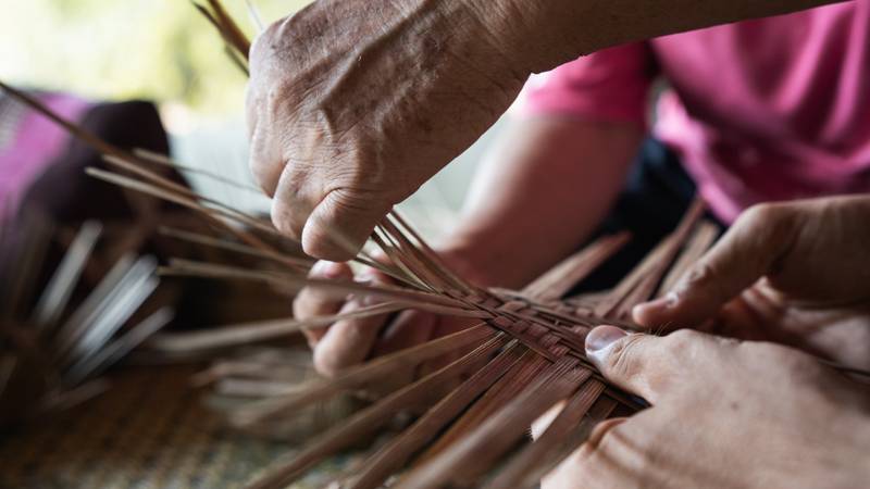 Artisan hands carefully weaving thin bamboo strips into traditional craft, showcasing local cultural experience available to guests — The Namkhan Luang Prabang