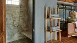 A teak ladder shelf holds folded grey towels beside a concrete wet-room shower.