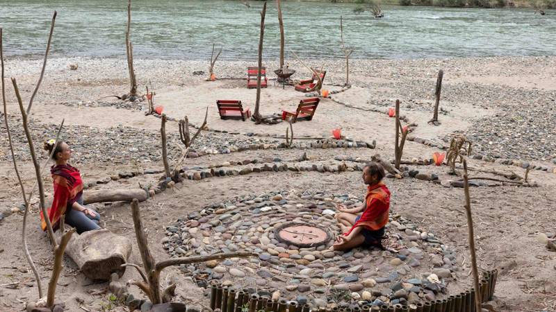 Two guests seated in contemplation within a spiral stone labyrinth on the Nam Khan riverbank, surrounded by driftwood sculptures and red lounge chairs