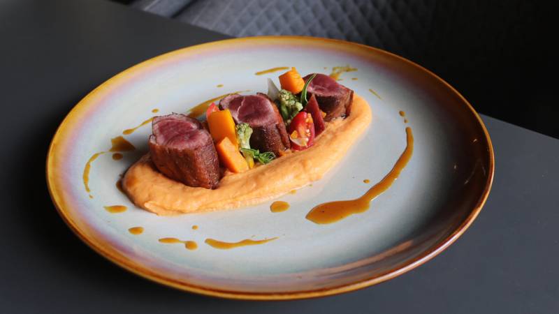 Perfectly seared duck breast medallions with glazed carrots, vibrant peppers, and smooth potato purée on artisan ceramic plate