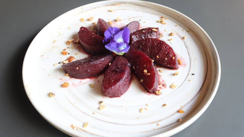 Artisan dessert plate featuring wine-poached plums garnished with purple edible flower and crushed nuts on ceramic dish