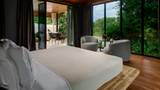 A neatly made king bed in a suite with floor-to-ceiling glass doors opening to a terrace and green jungle beyond.
