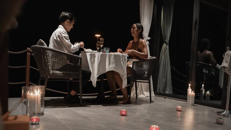 Couple enjoying private candlelit dinner on villa terrace at night with decorative lanterns and wooden ceiling at Namkhan resort