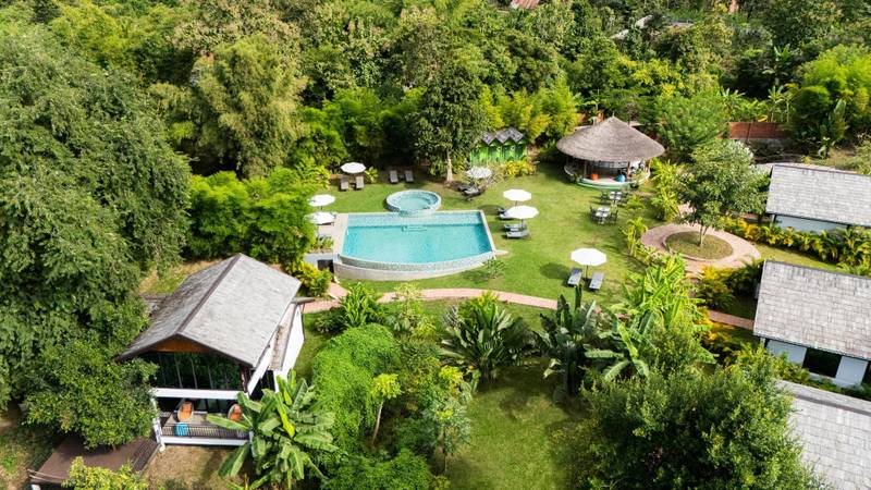 Aerial view of The Namkhan resort pool surrounded by lush tropical gardens and traditional Lao architecture in Luang Prabang, Laos