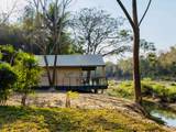 Canvas tent on stilts beside the Nam Khan river at The Namkhan eco-resort in Luang Prabang, Laos, surrounded by tropical vegetation.
