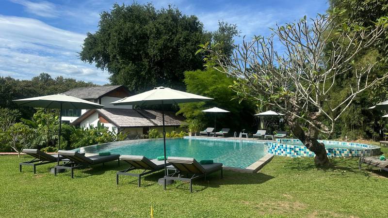 Infinity pool surrounded by sun loungers and tropical gardens at The Namkhan resort in Luang Prabang, Laos, with clear blue skies overhead