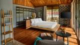 A teak-floored suite with a low platform bed, open wardrobe, and large sliding glass doors to a terrace.