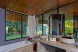 Spacious bathroom at The Namkhan resort in Luang Prabang featuring dual stone vessel sinks, soaking tub, and floor-to-ceiling windows overlooking lush garden...