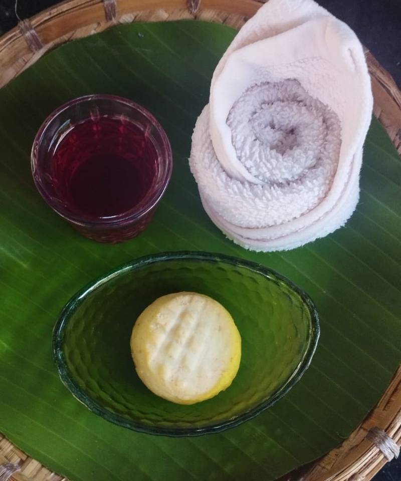 Bamboo tray with rolled towel, herbal compress in glass bowl, and traditional Lao spa beverage on banana leaf at Namkhan resort