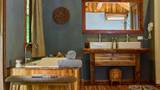 A soaking bathtub with rolled grey towels beside a teak vanity and rattan basket.